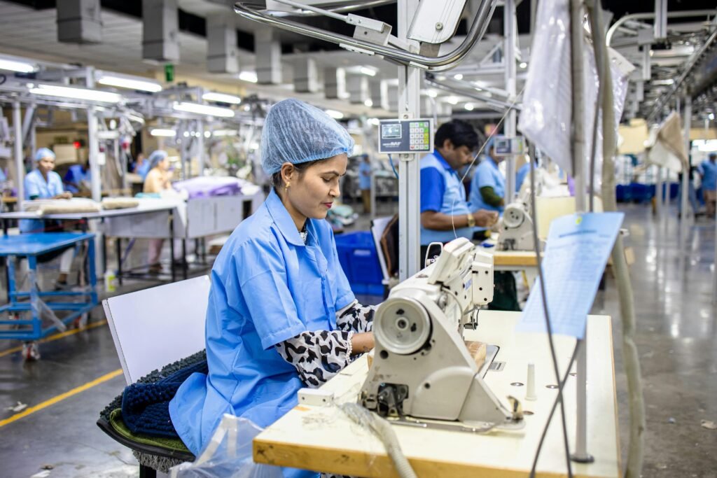 Workers in a textile factory operating sewing machines, wearing blue uniforms and hairnets, focused on their tasks.